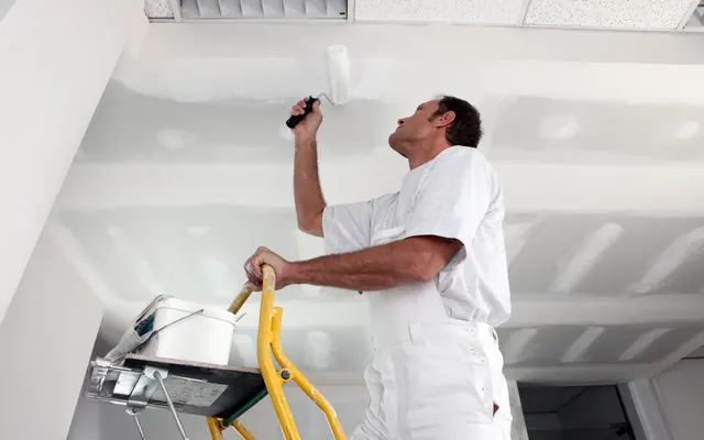 Painter rolling white paint onto a ceiling