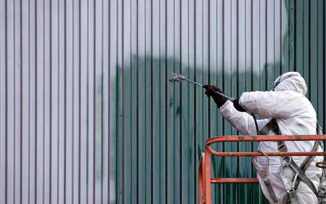 Painter spraying a metal warehouse wall from a lift